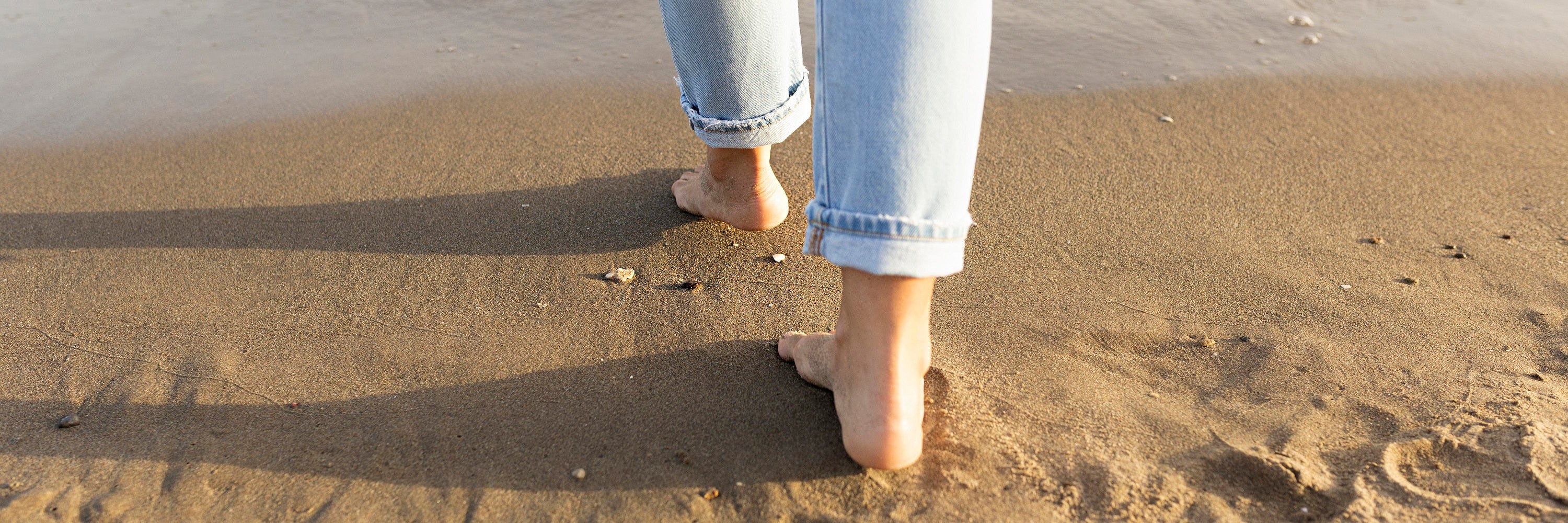 A woman's feet are standing on a sandy beach - Joyo barefoot