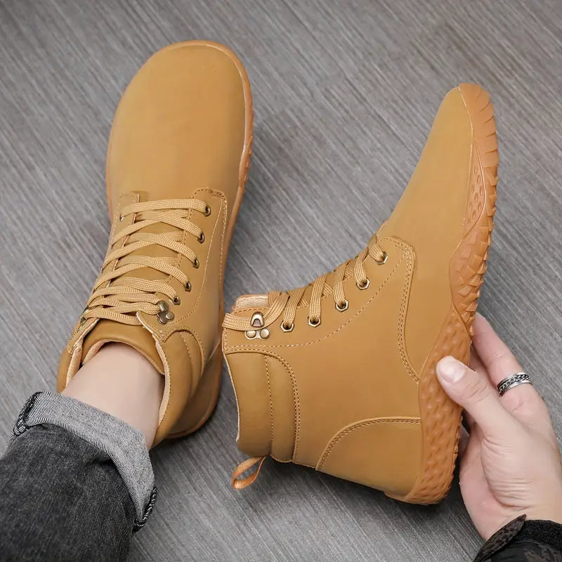A hand holding a pair of brown boots - Joyo barefoot